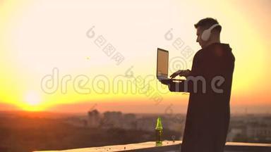 日落时分，一个戴着耳机的自由职业者站在屋顶上写着键盘代码页。 <strong>小生</strong>意。 听着听着